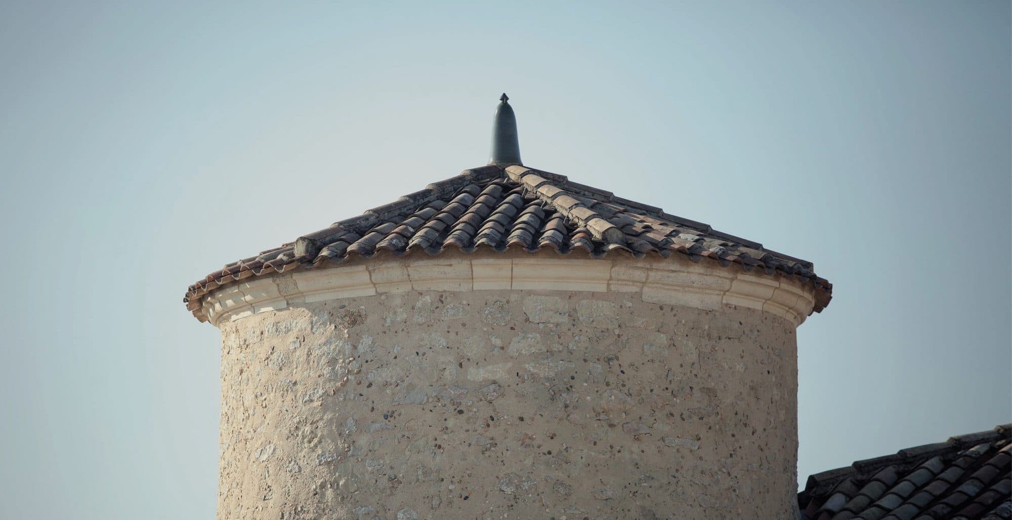 The pale stone tower of Château Lafaurie-Peyraguey at midday, vineyard rows running to the foot of its walls.