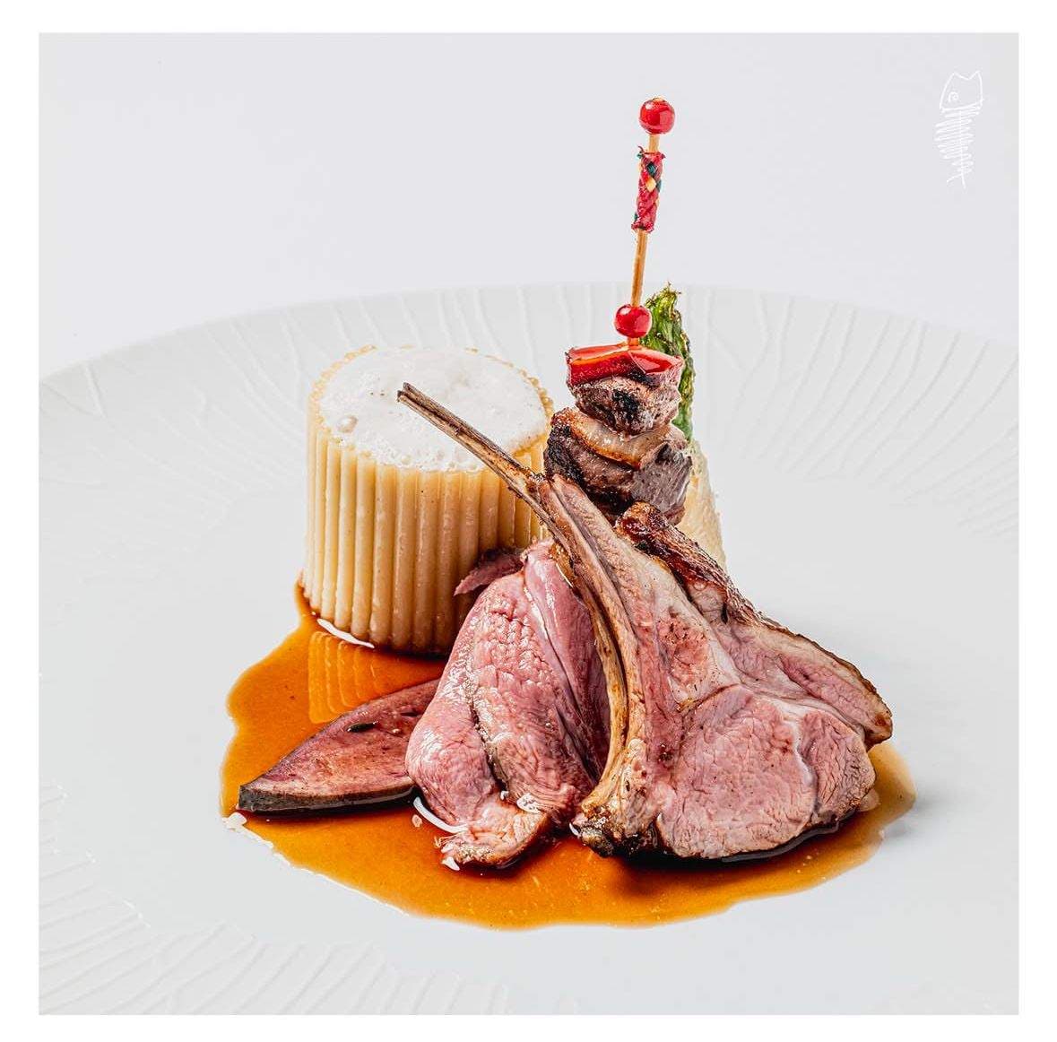 A plate of Catalan lamb — a rosy rack of three trimmed cutlets, a tall fluted rigatoni gratin foamed over with mushroom cream, a single Languedoc skewer of red berries and grilled vegetable on the side.