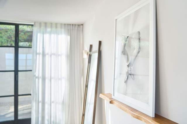 An interior moment in a suite — a framed work, sheer curtains, the door to the garden ajar.