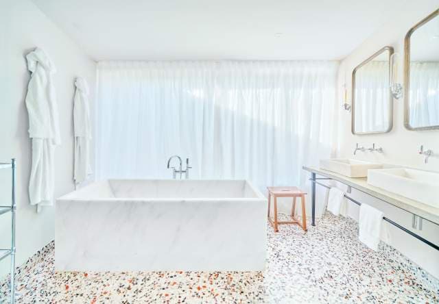 A marble bath in a Villa La Coste suite, terrazzo floor and full-length linen at the windows.