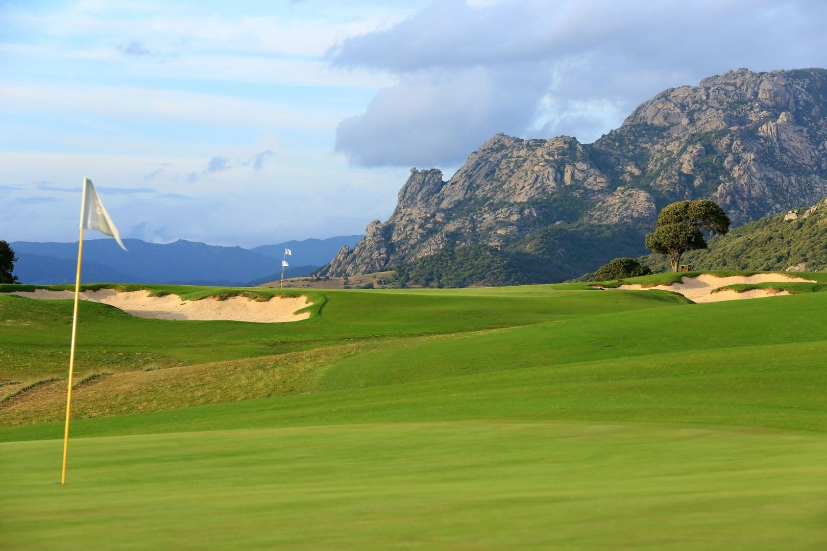 The Murtoli golf links — a fairway running toward the dramatic granite peaks of the Alta Rocca, sand bunkers in the middle distance.