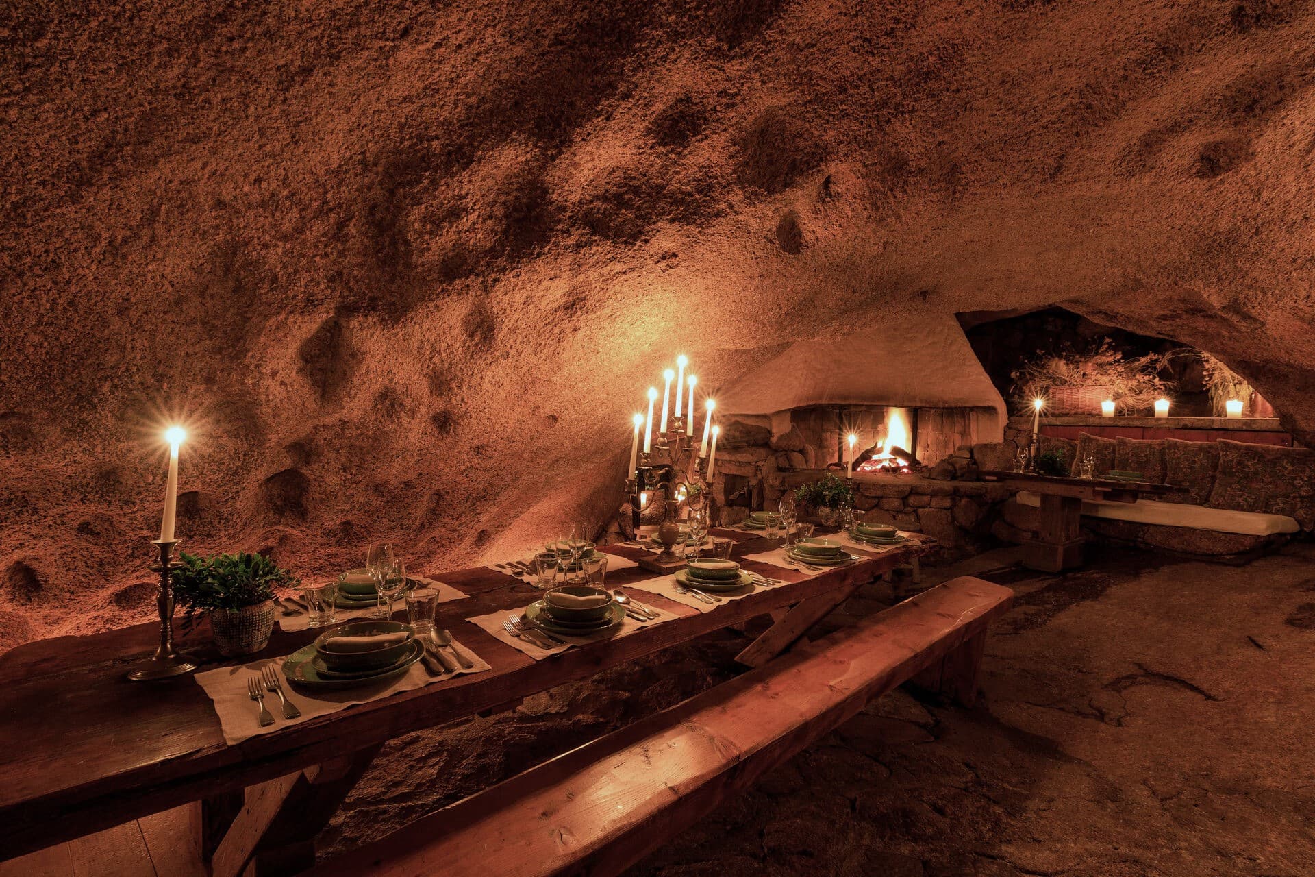 Dinner at La Grotte — a long candlelit table laid inside a granite cave, the rock walls warmed amber by lantern light.
