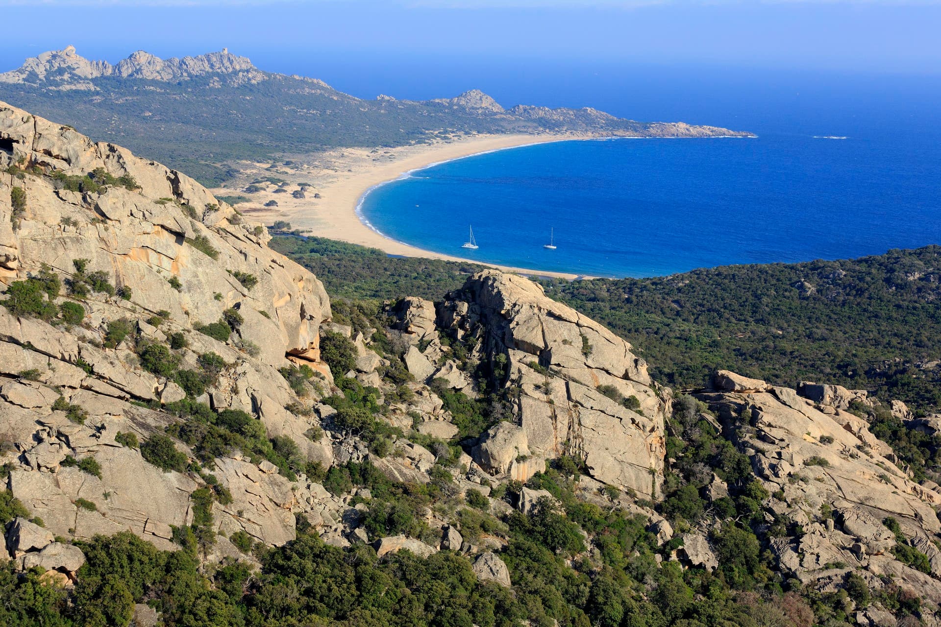 The estate seen from the headland — granite cliffs, the maquis dropping away to a wide curve of pale sand and the open sea beyond.