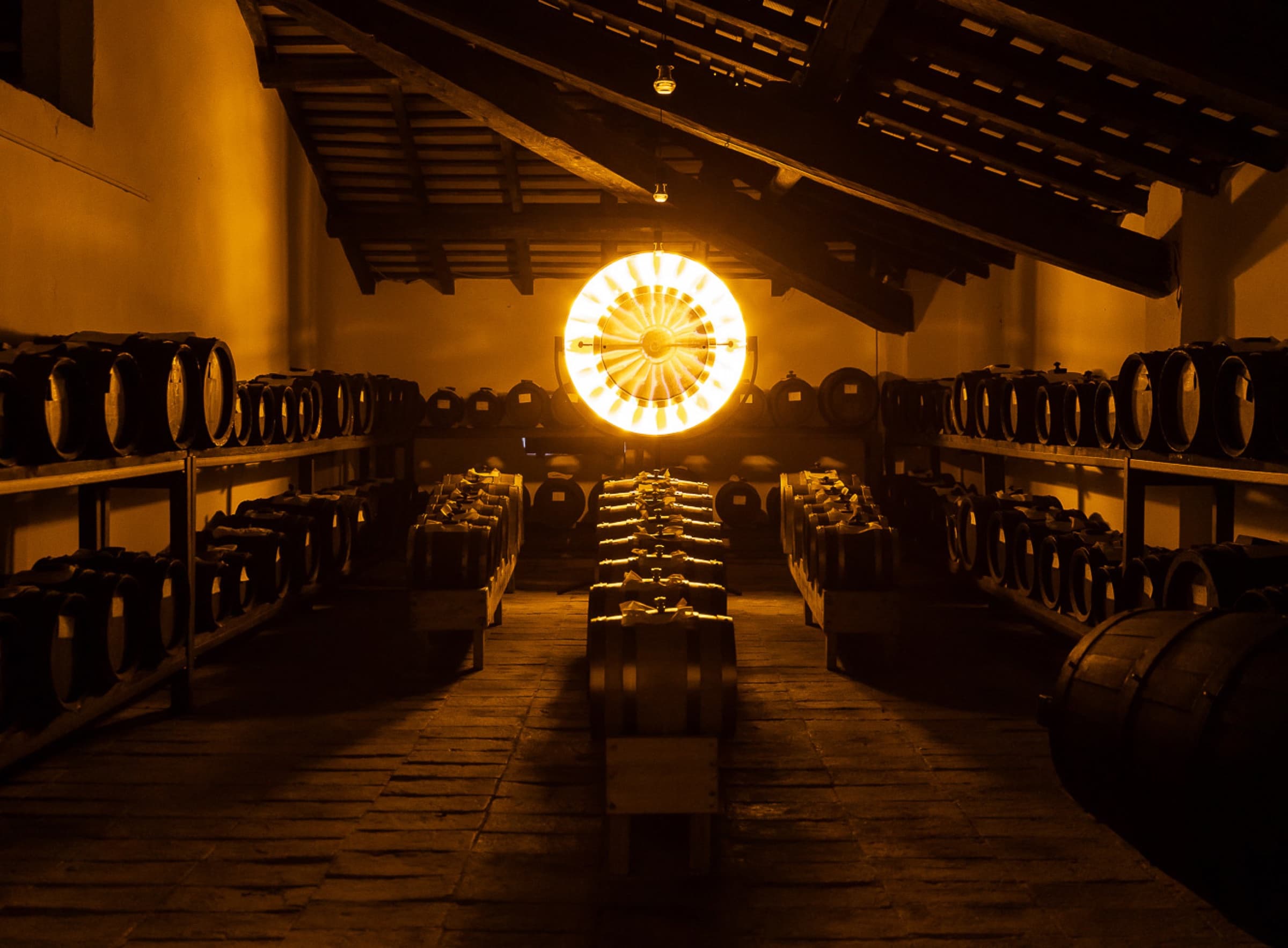 Massimo Bottura in low light drawing balsamic from a barrel with a long glass pipette, the dark brown liquid catching the light.
