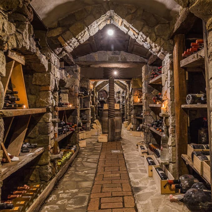 The wine cellar at Quattro Passi — a barrel-vaulted tunnel of rough volcanic stone with a brick floor and timber racks of bottles down both sides, a single lit lantern overhead, an old wooden press at the far end.