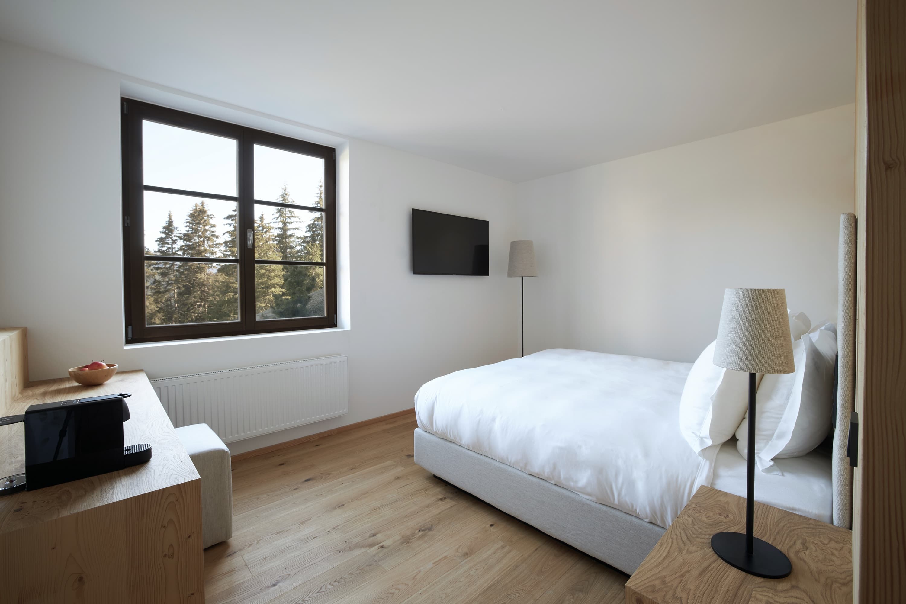A tower suite in pale oak and white linen — a deep window framing nothing but spruce tops and sky.
