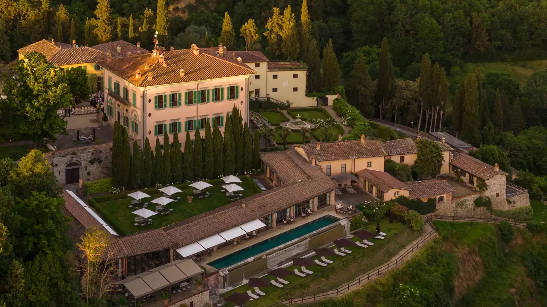 The Dimora Storica from the air — the historic 1854 villa above its formal parterre and the terraced pool, set into cypress and olive.