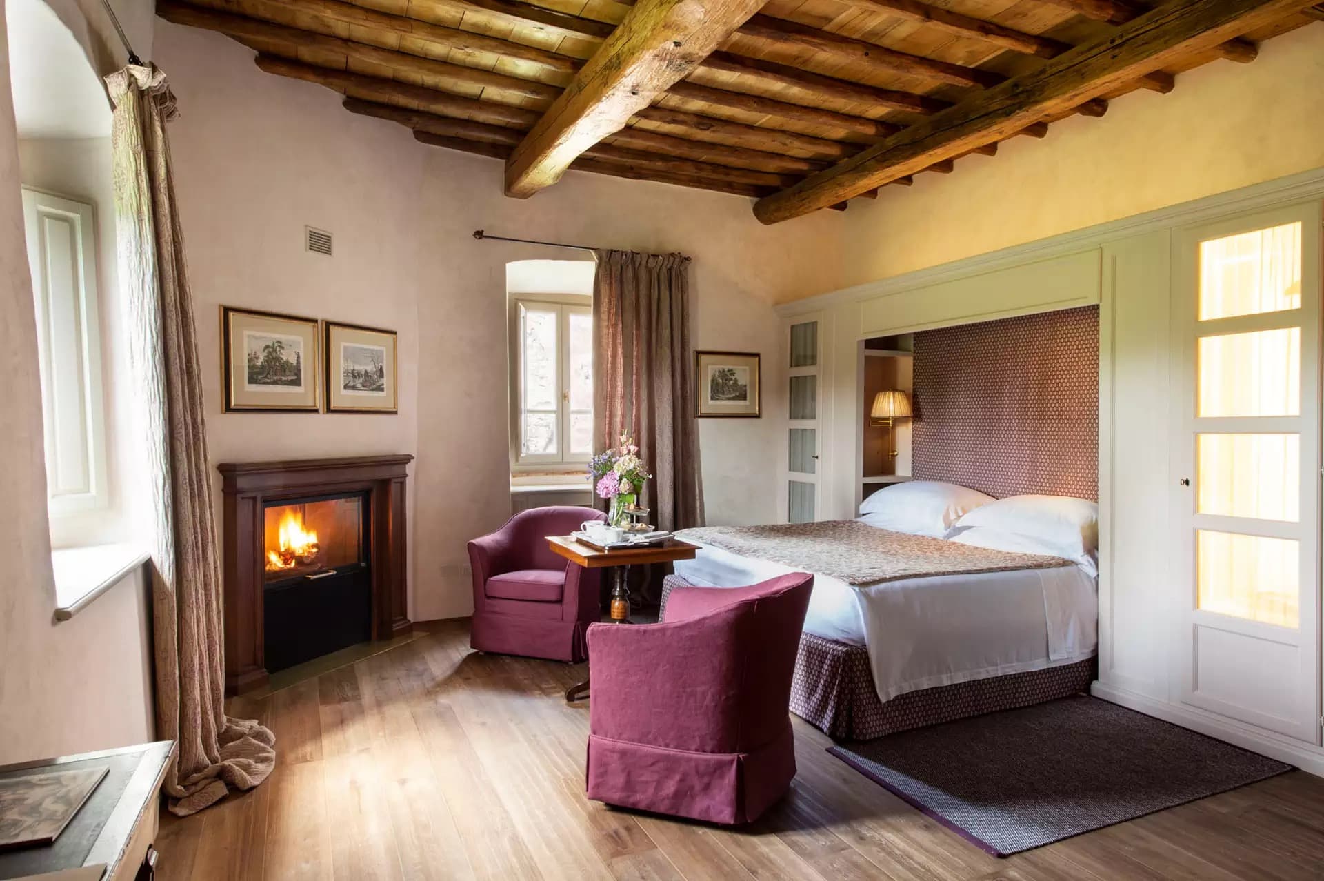 A village suite with a chestnut-beamed ceiling, an open fire and a pair of plum-velvet armchairs at the foot of the bed.