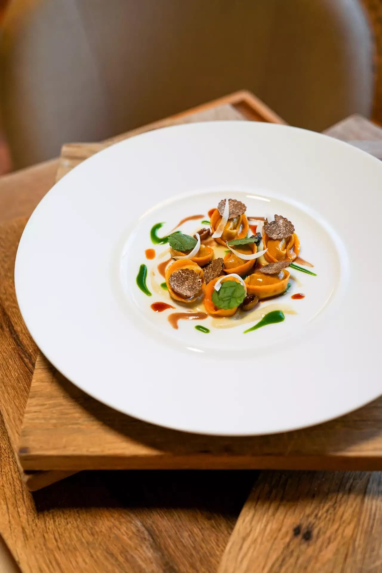 A wide white plate of small tortelli ringed with cream, finished with shavings of black truffle and a leaf of mint.