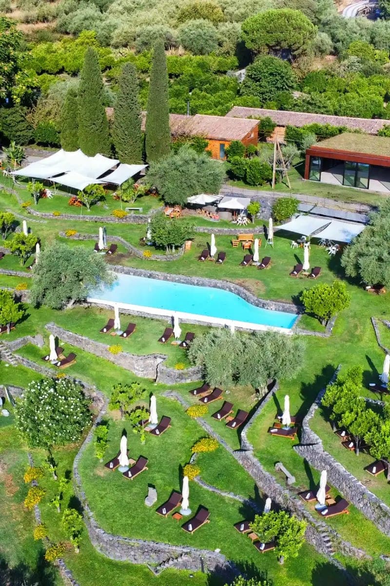 A vertical view of the estate's pool, water held against black-stone terraces and citrus trees.