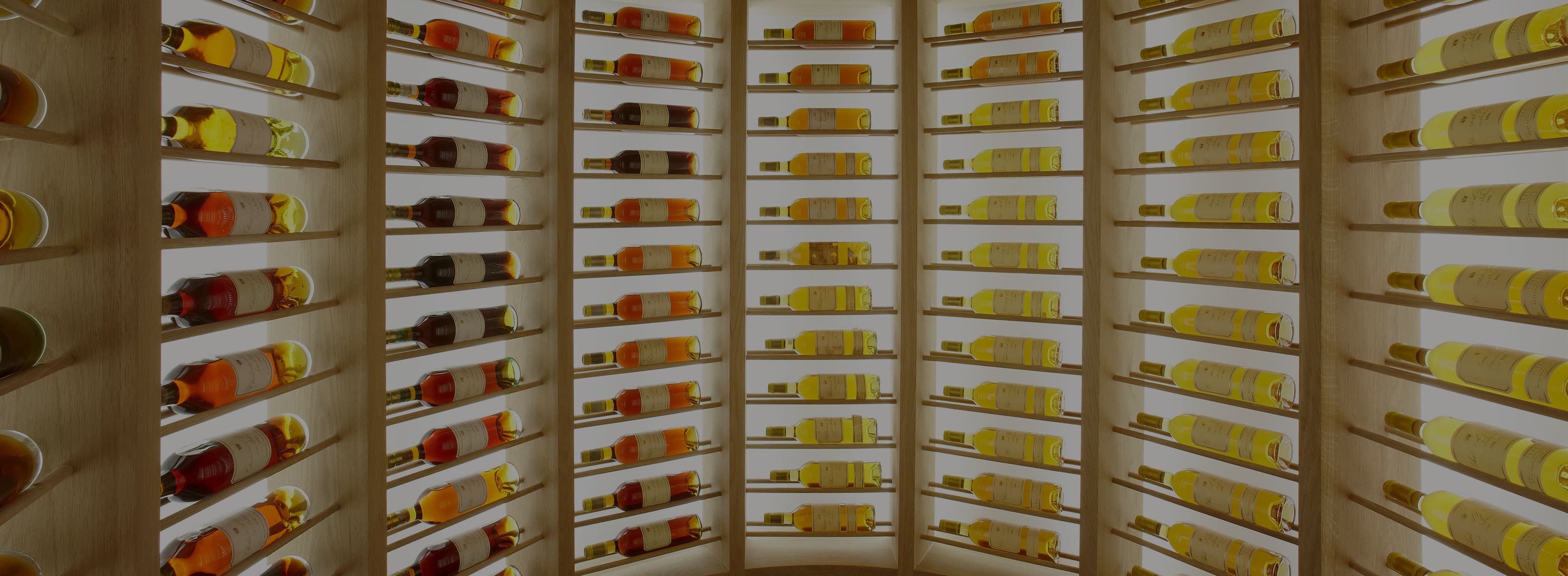 A long wall of Château d'Yquem — bottles laid flat on pale-wood racks, the labels reading vintage after vintage from rose-gold to deep amber.