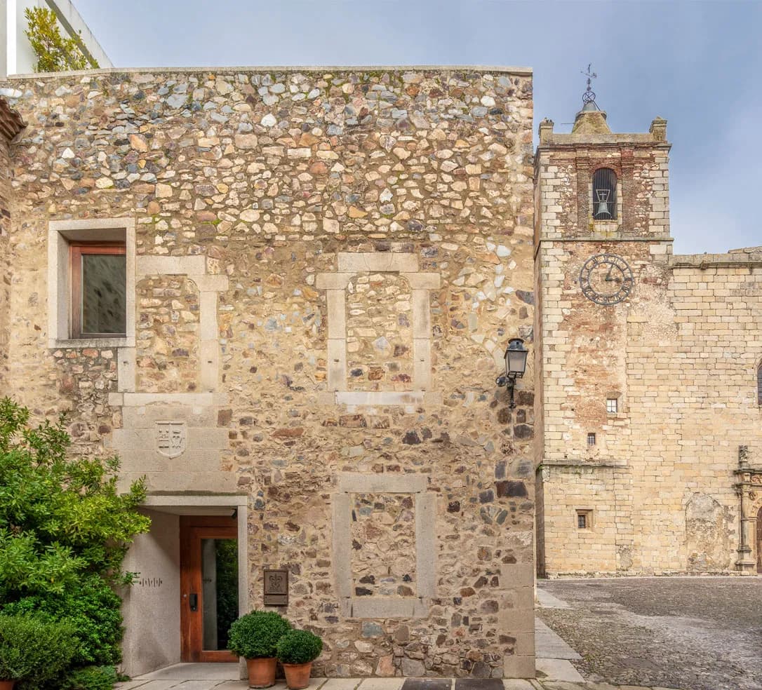 The Atrio facade in old Cáceres — a plain granite wall, a small dark door, the bell tower of San Mateo rising behind.