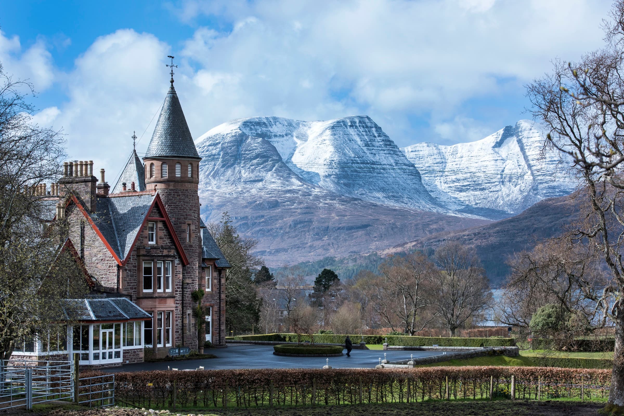 The red sandstone lodge with its turret and conservatory in the foreground, the snow-streaked summit of Liathach rising directly behind it.