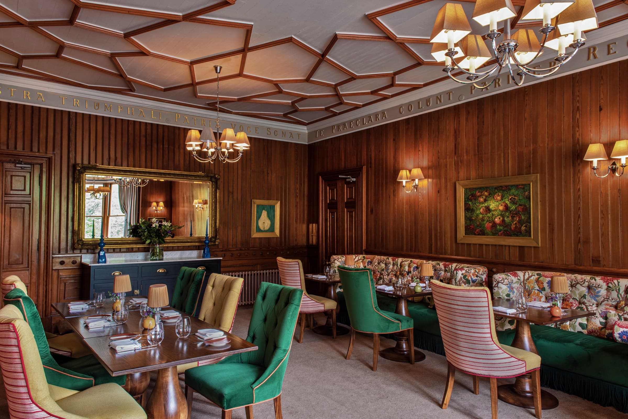 The 1887 dining room — wood panelling, a coffered ceiling, green velvet chairs around dressed tables, a tapestry banquette along the far wall.