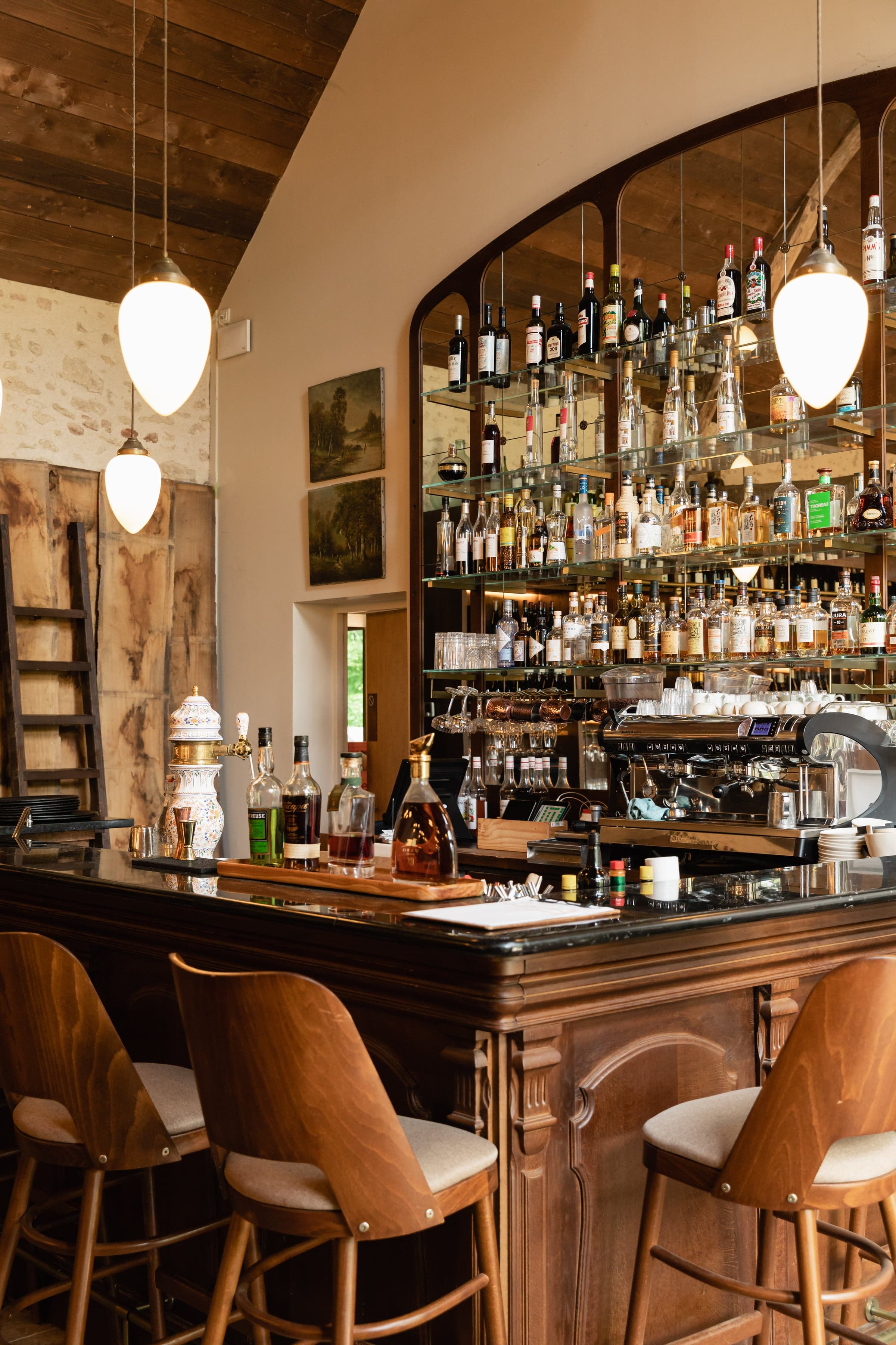 The bar at the manor, dark wood shelves stacked with bottles and glassware behind a low counter.