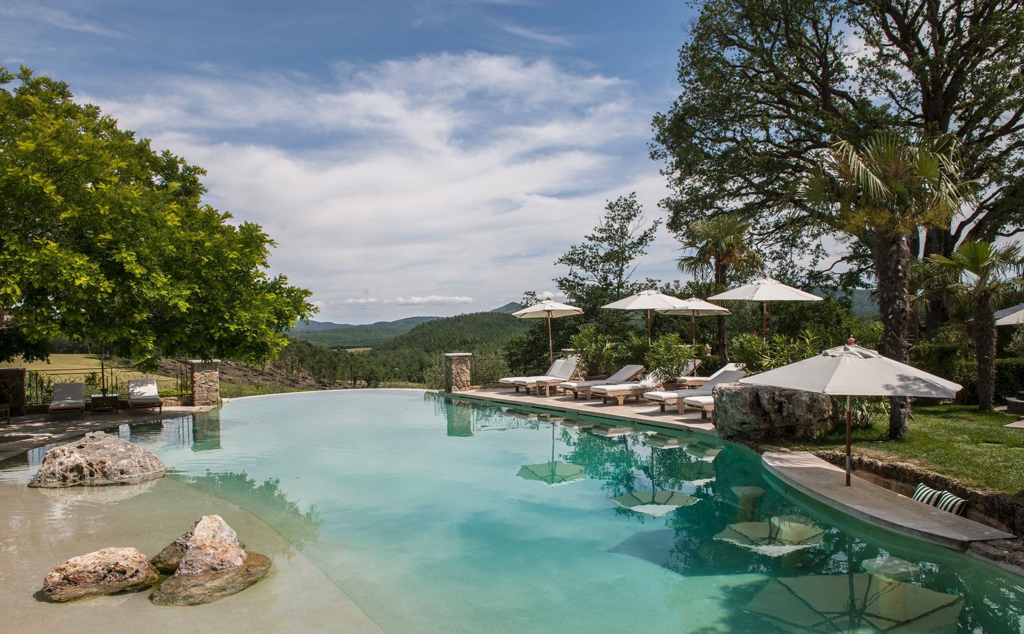 The infinity swimming pool at Borgo Santo Pietro, lounge chairs and parasols set against the Tuscan hills.