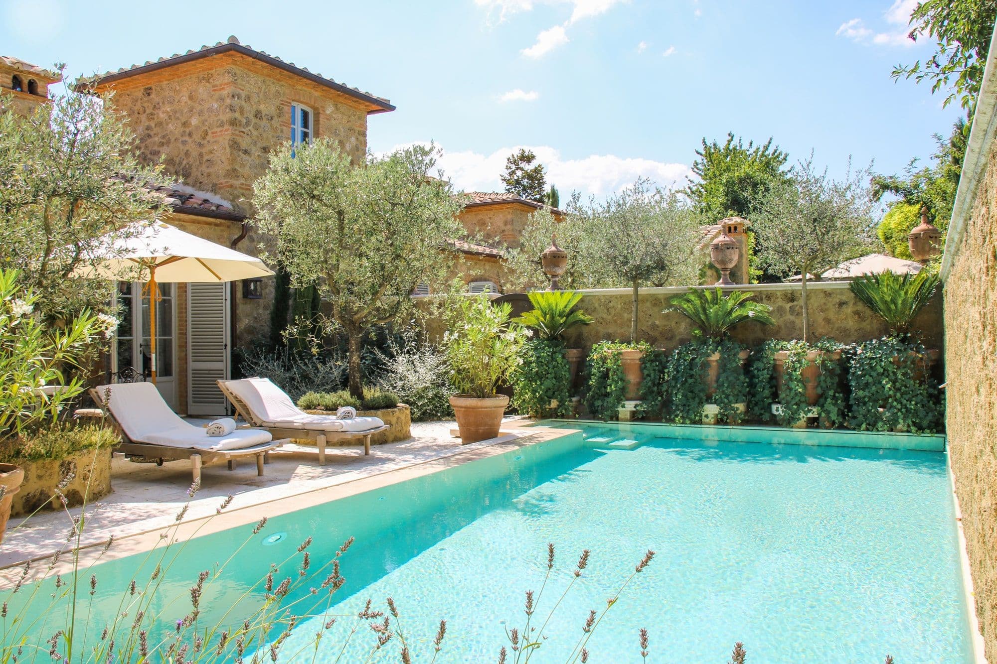 A private pool suite at Borgo Santo Pietro — a small terrace pool, lavender and olive trees, the borgo's stone walls behind.
