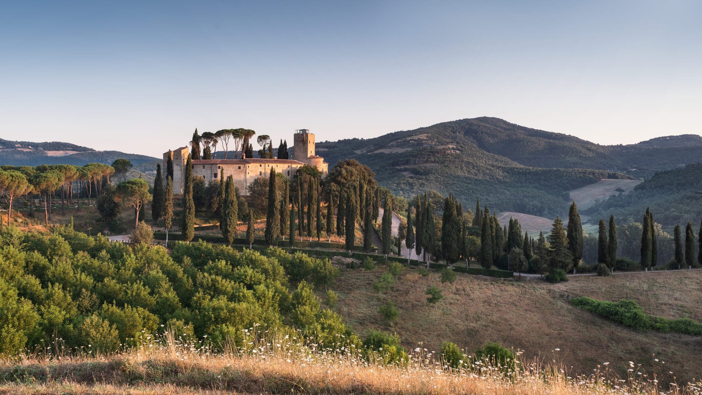The Castello di Reschio above its Umbrian hills at midday, stone walls rising over the olive groves.