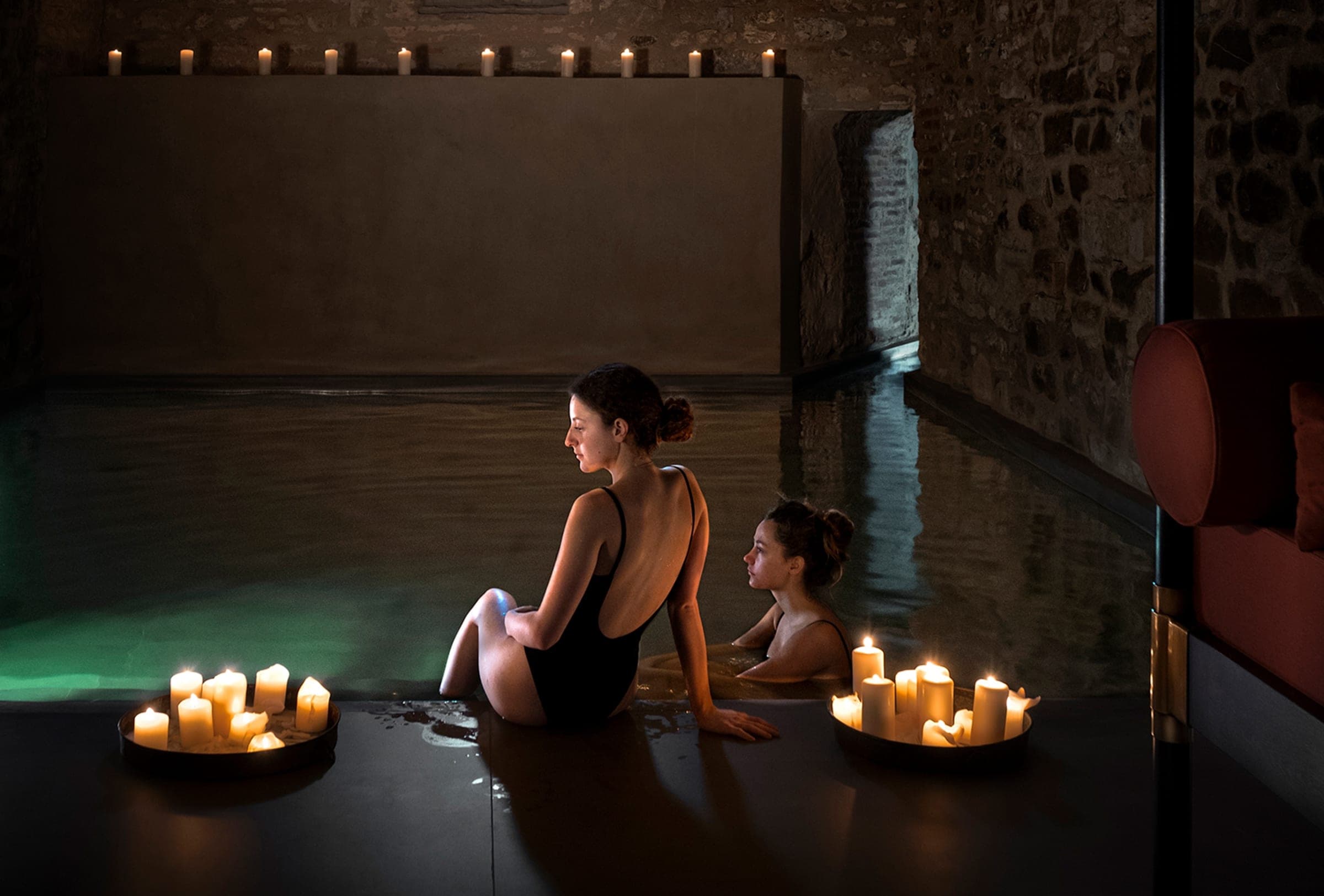 The vaulted bathhouse beneath the castle, candlelight on warm stone and still water.