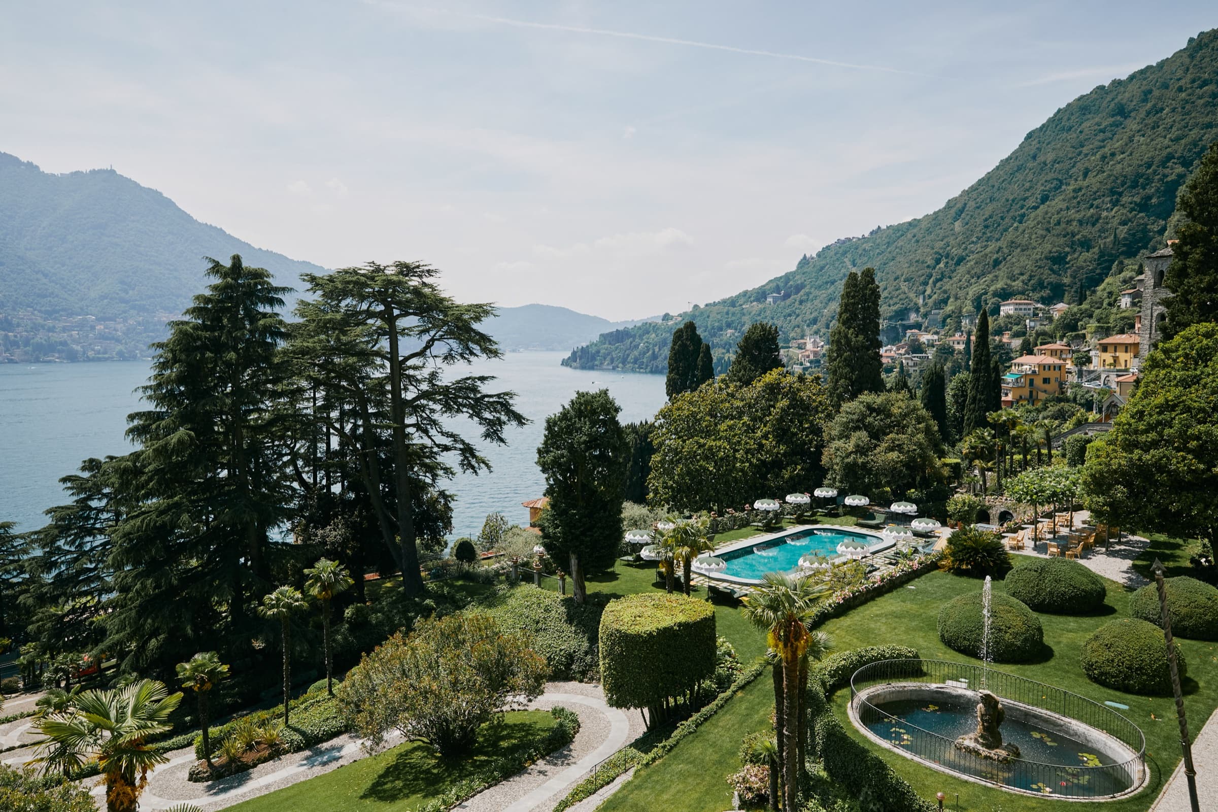 An aerial view of Passalacqua's terraced gardens, the outdoor pool and parterre fountains laid out between cedars and cypresses, Lake Como and the western shore beyond.