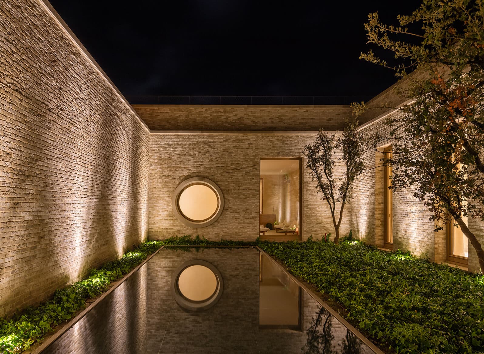 The Santuario spa courtyard at Abadía Retuerta at night — limestone walls, a circular window above a still reflecting pool.