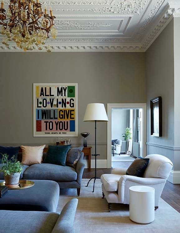 The drawing room, low lamplight on framed paintings and a pair of armchairs angled toward the fire.
