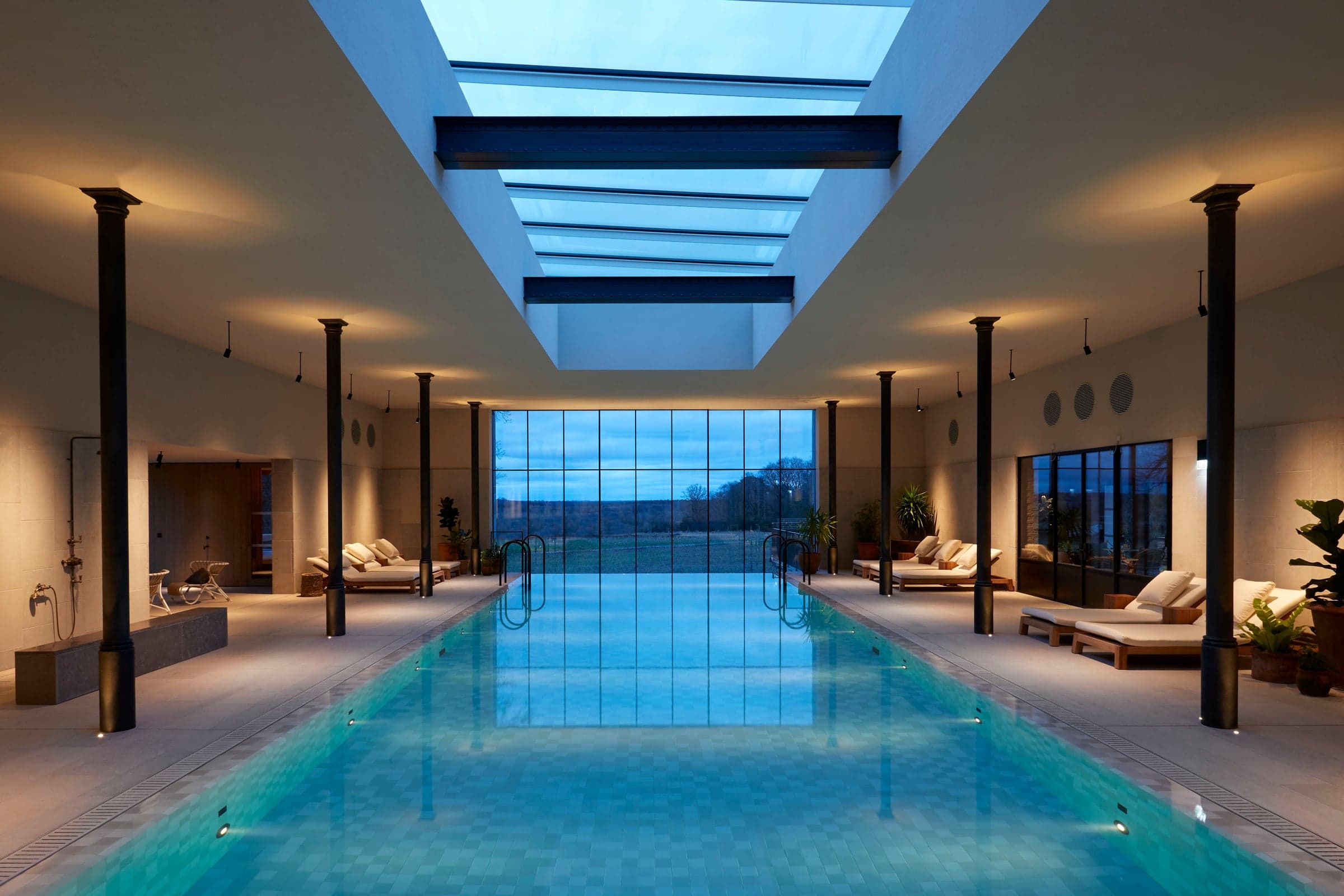 The indoor pool at the Bothy, low light reflected on the water, white timber and stone above.