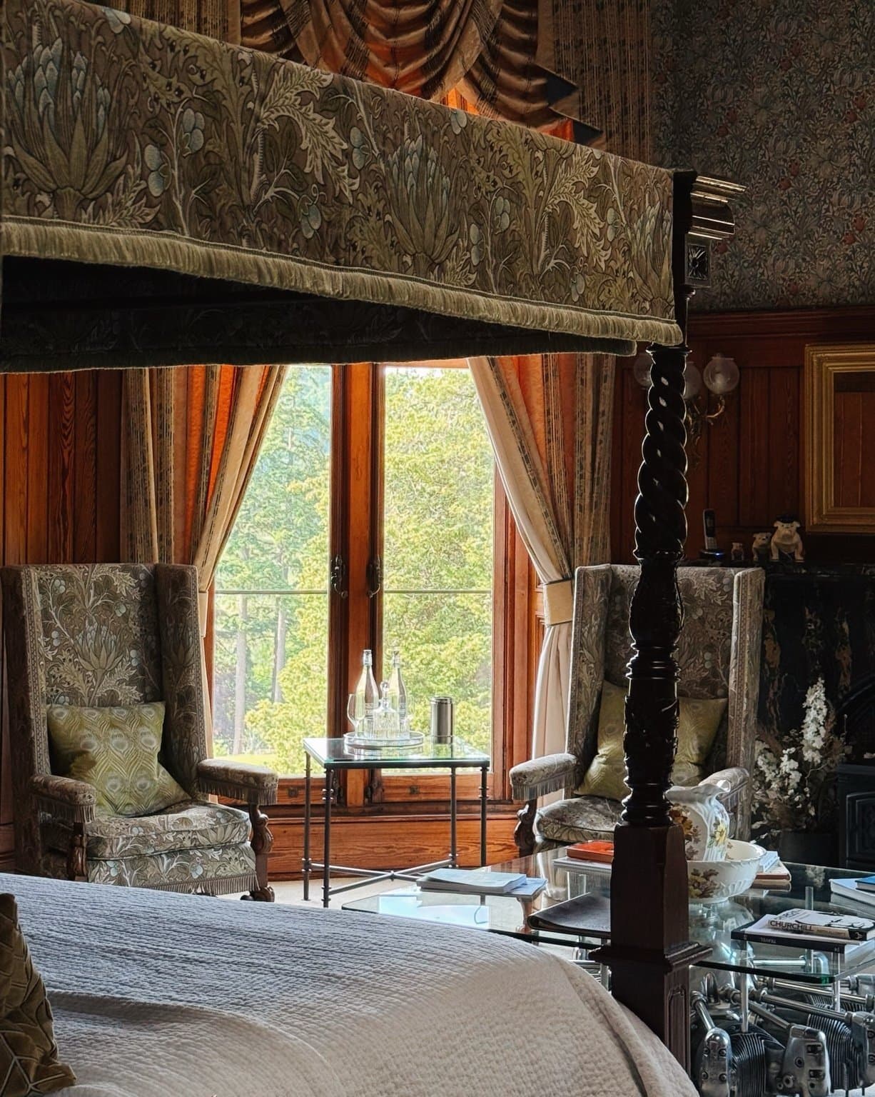 A four-poster bed in the Churchill Suite, deep curtains and a tall window onto the garden.