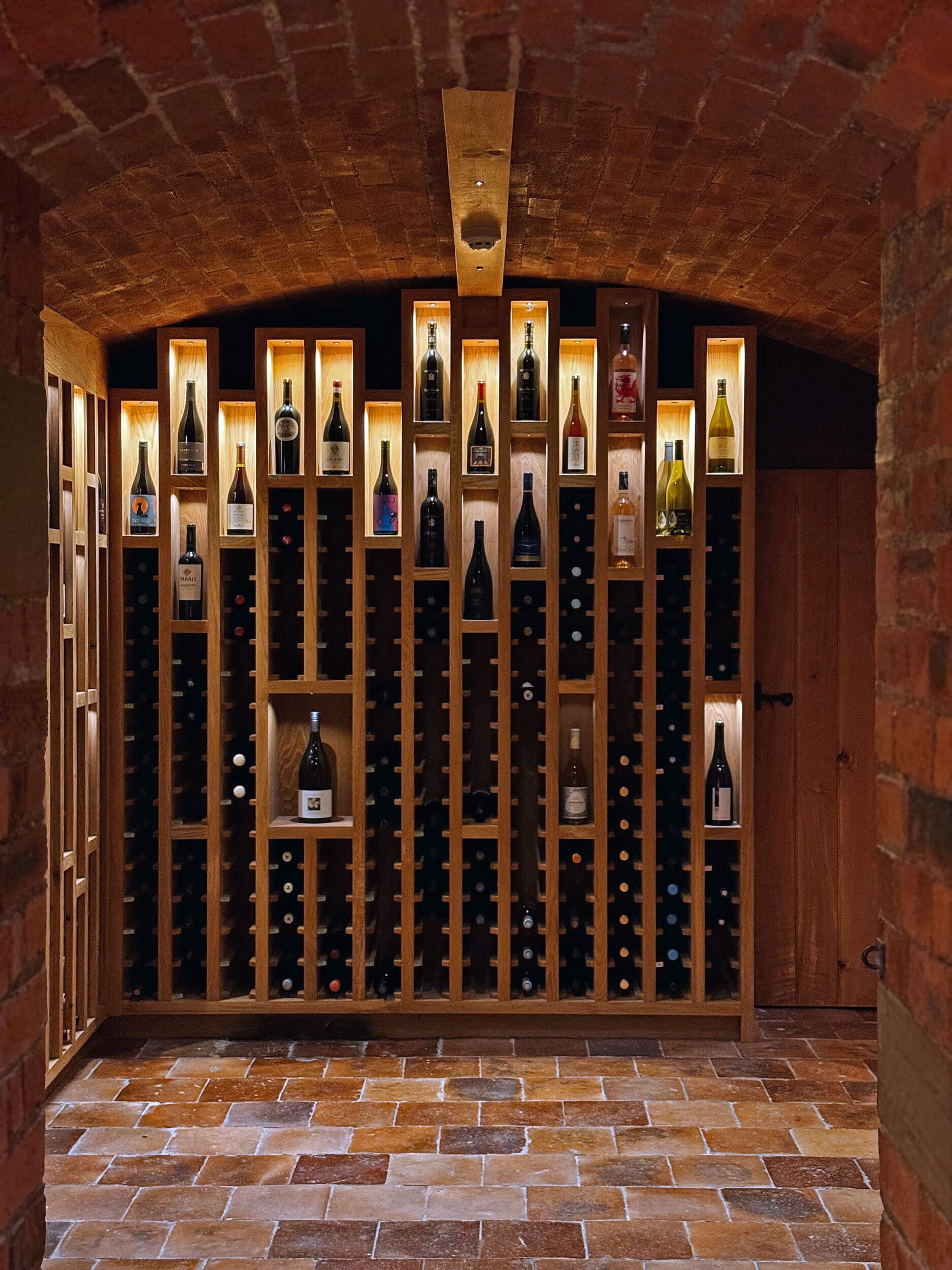 The barrel-vaulted wine cellar, bottles lit between oak racking on a brick-laid floor.