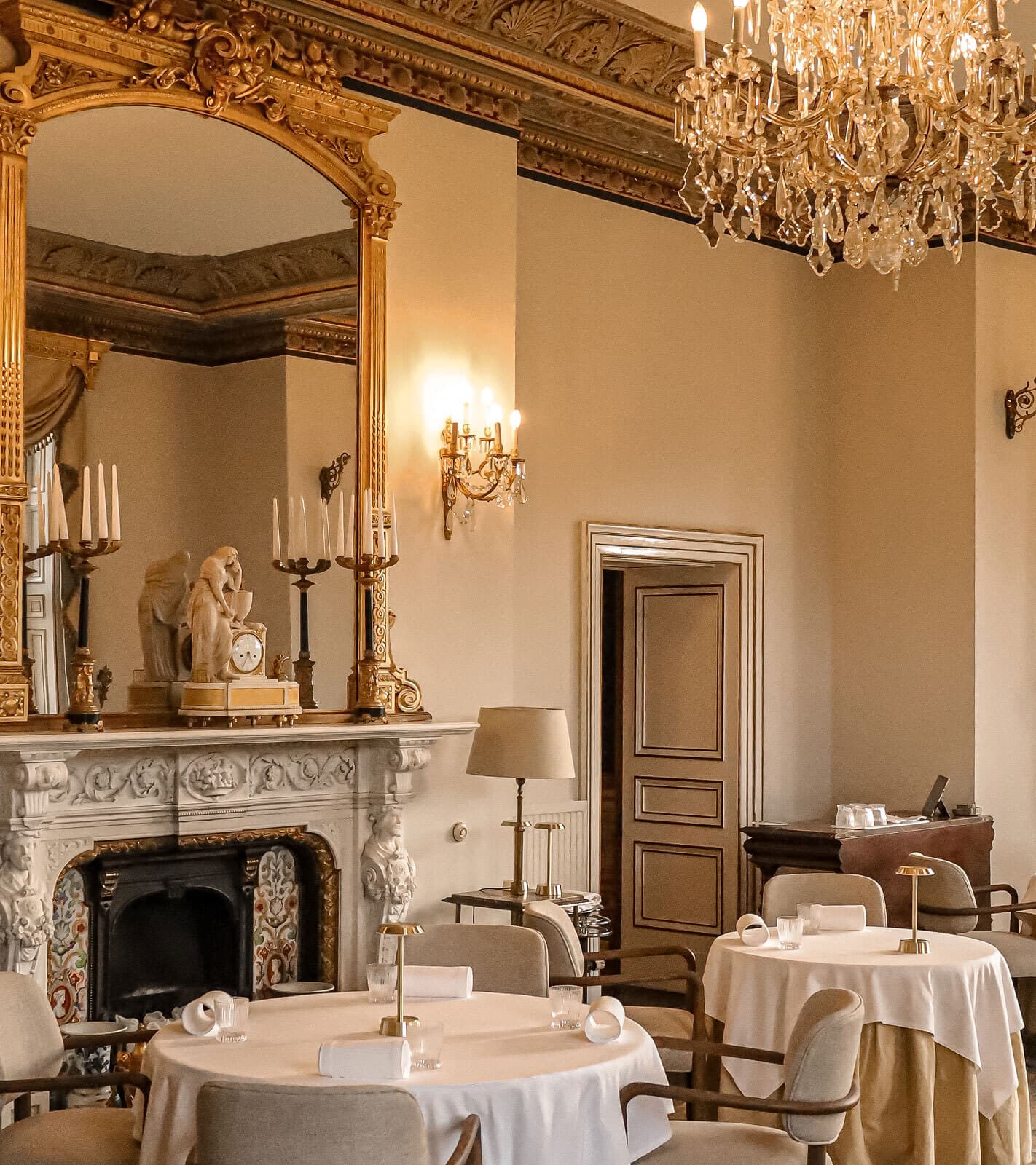 The Henry Robertson dining room at Palé Hall — gilded mirror, marble fireplace, round tables set with white linen.