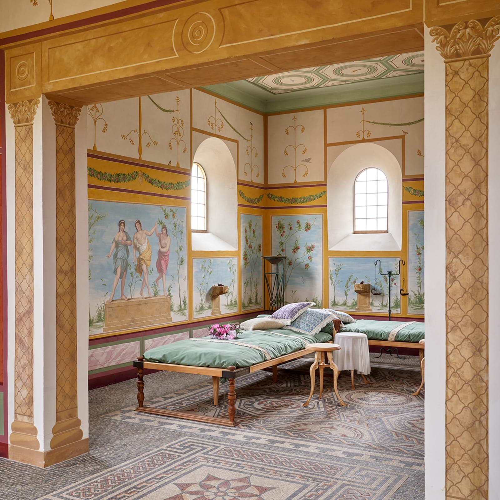 The reconstructed interior of the Roman villa, frescoed walls in soft greens and ochres above mosaic floors and a pair of ceremonial daybeds.